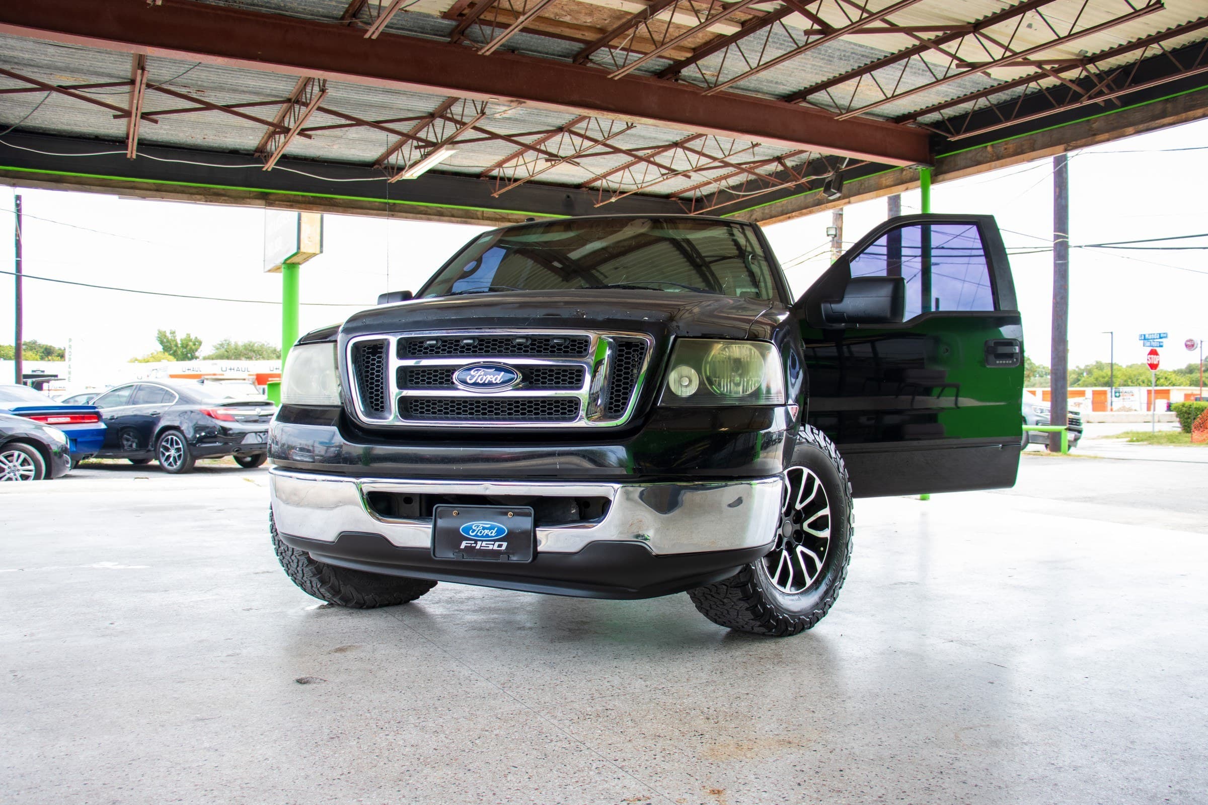 Front driver-side view of the black F-150 with the driver's door open, showing the chrome front bumper and black machined-face alloy wheels.