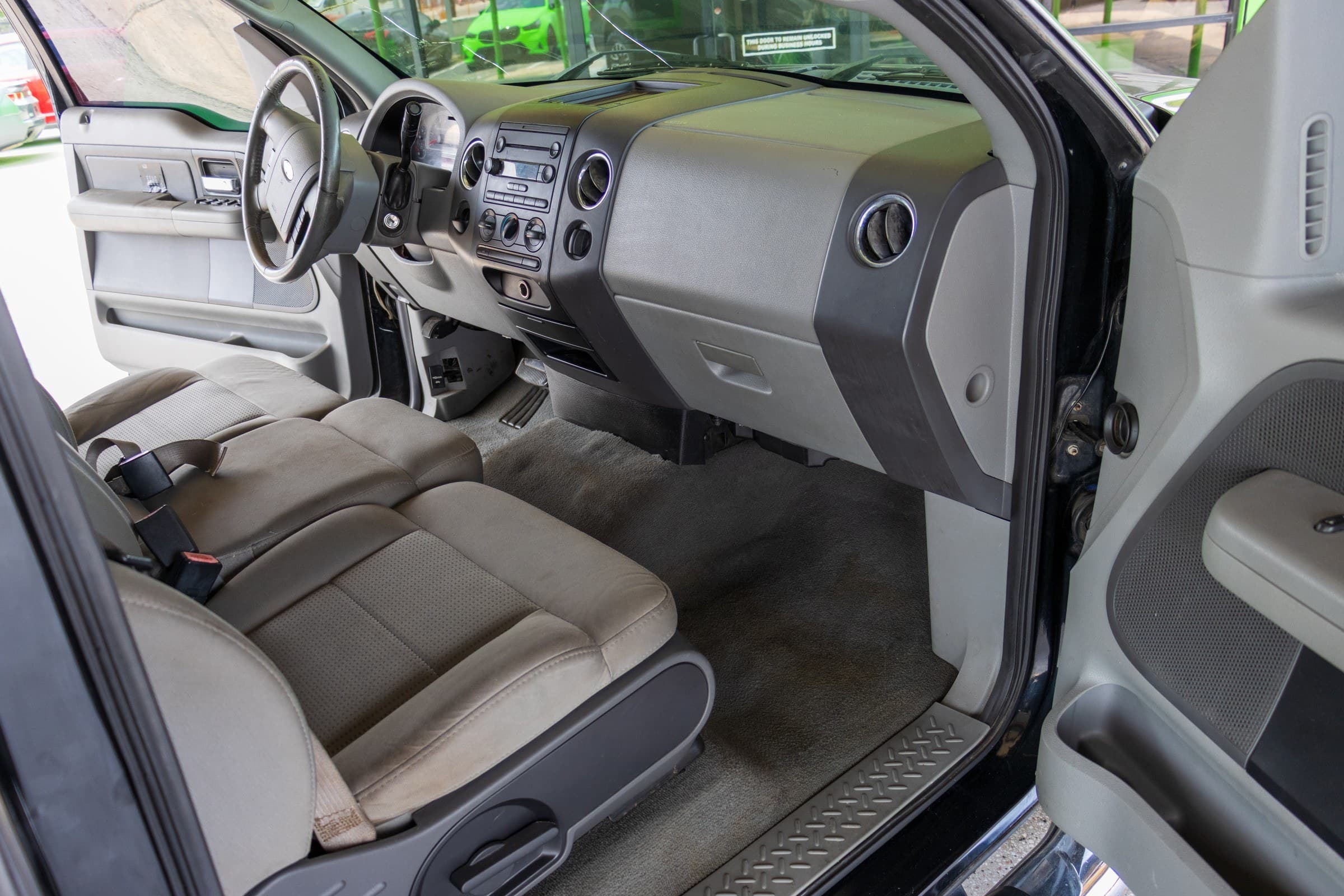 F-150 front cabin seen through the open passenger door, showing the gray dash, center stack radio and tan cloth front seat.