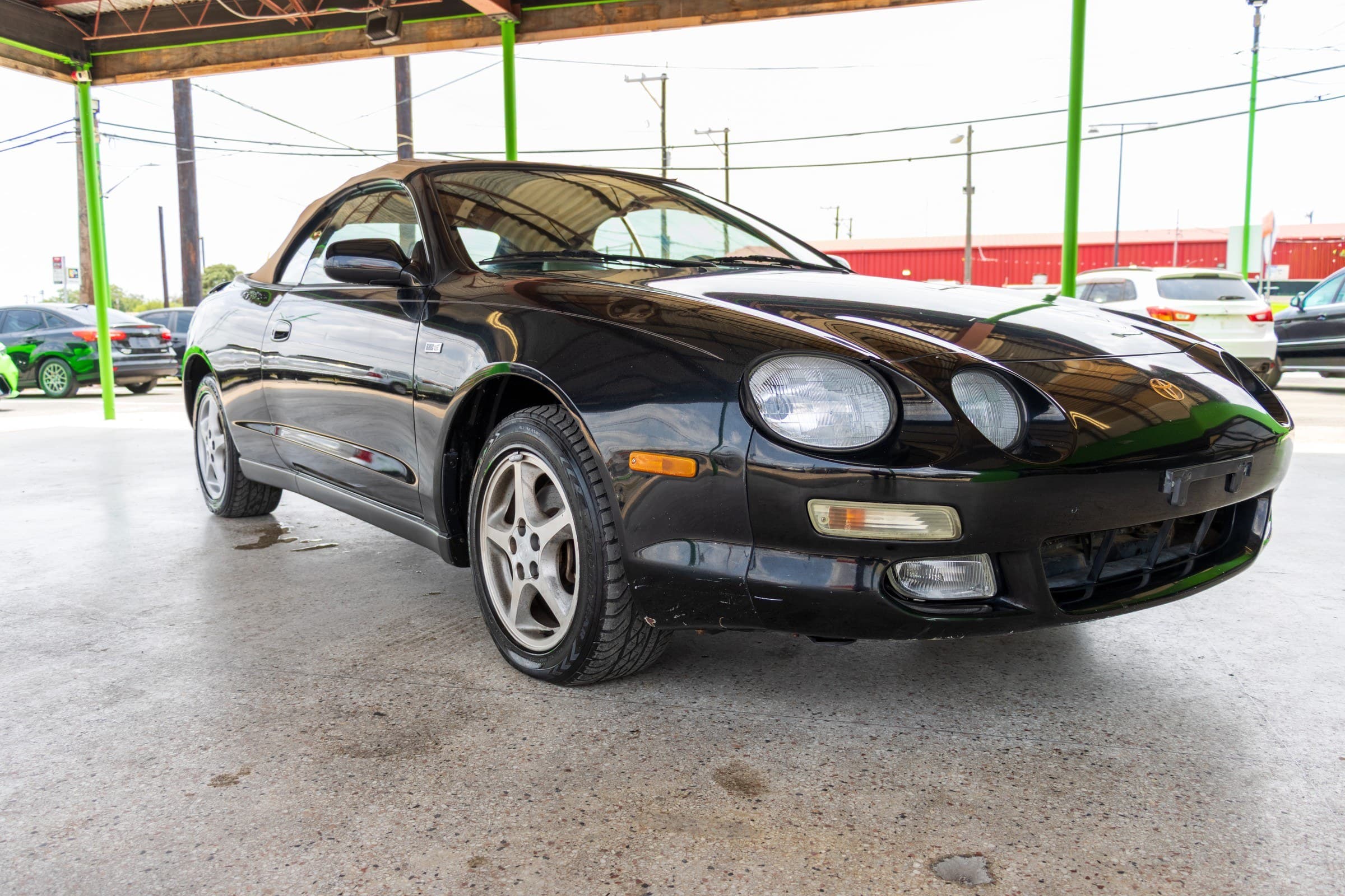 Black 1997 Toyota Celica GT convertible with its tan soft top raised, seen from the front passenger side.