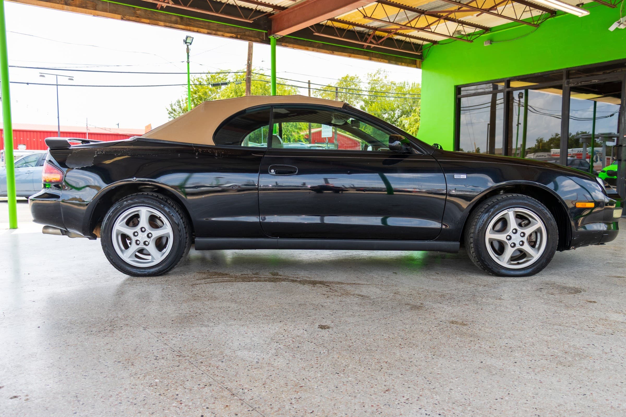 Passenger-side profile of the Celica convertible with the tan top up, showing the rear spoiler and silver five-spoke alloy wheels.