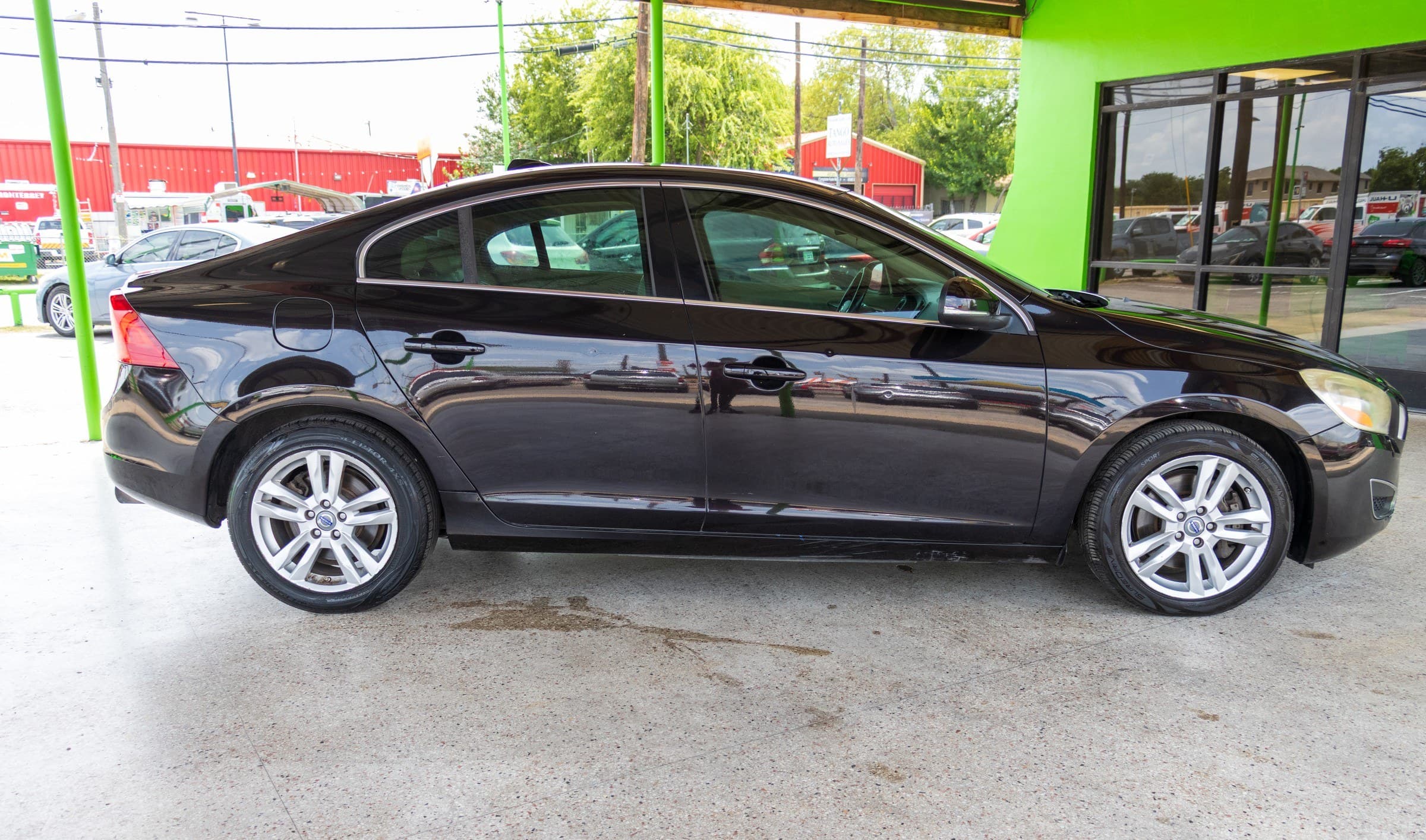 Full passenger-side profile of the black Volvo S60 parked under the Kelley Autoplex canopy.