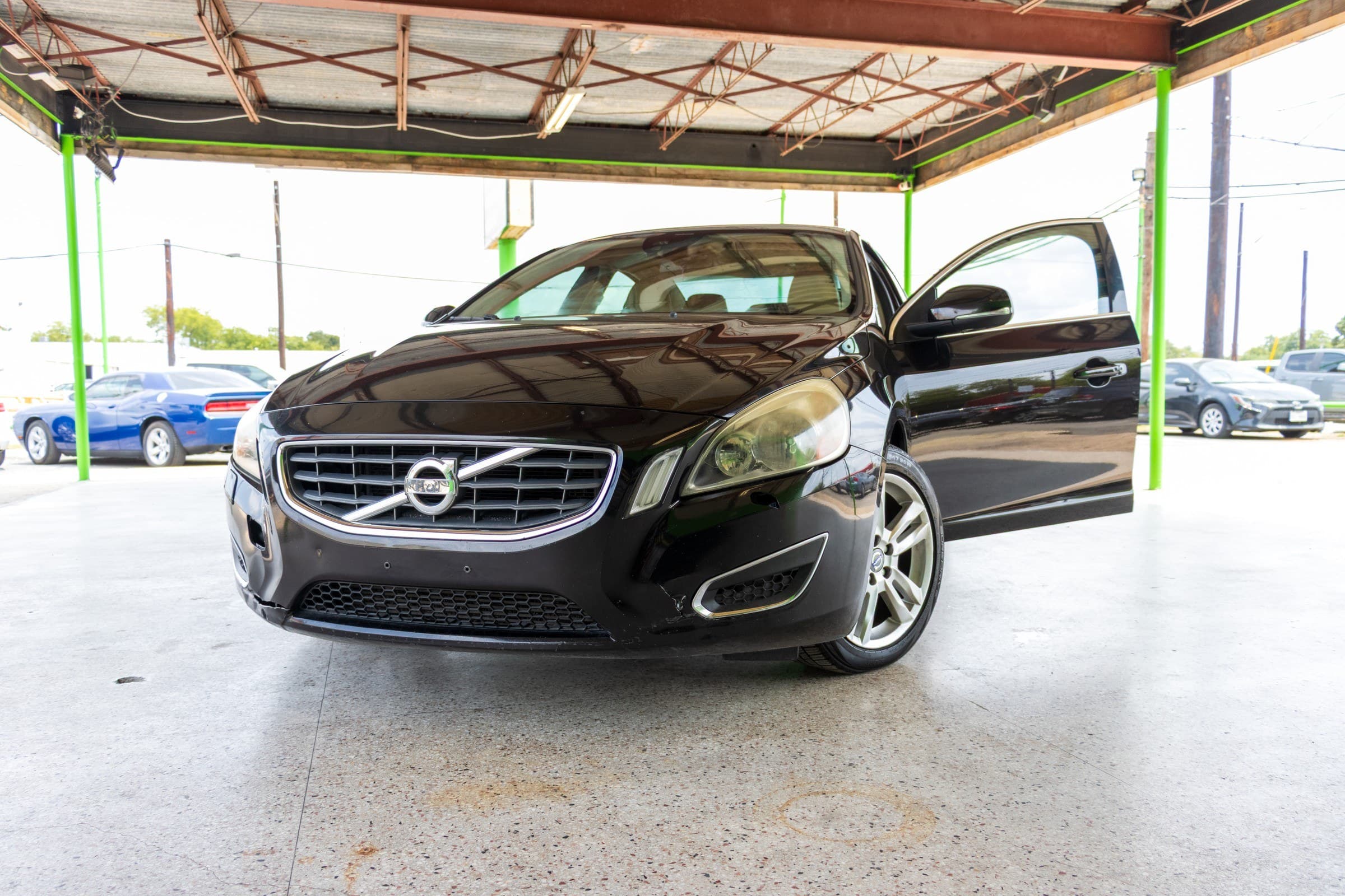 Black 2013 Volvo S60 T5 seen from the front with the driver's door open, showing the chrome-ringed grille and Volvo badge.