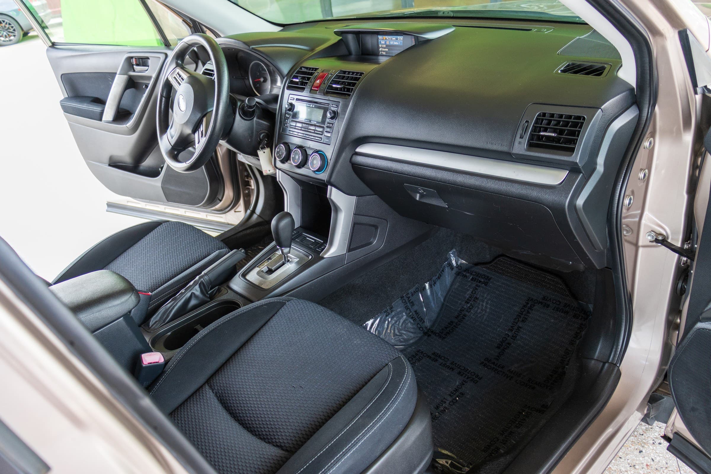 Forester cabin seen through the open passenger door, showing the black dashboard, centre stack and the automatic gear selector.
