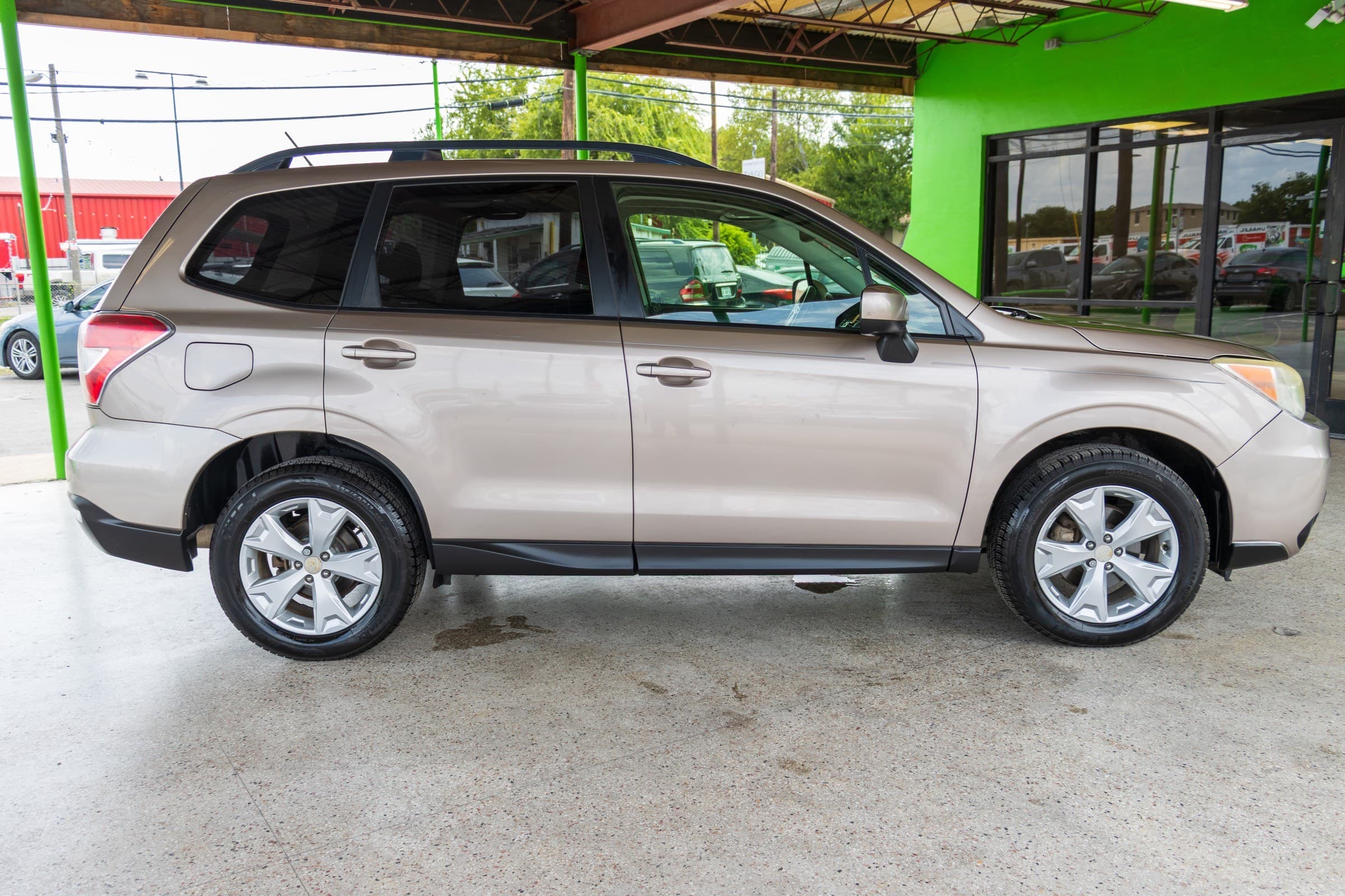 Full passenger-side profile of the bronze Forester, showing the black roof rails, body-coloured door handles and silver alloy wheels.
