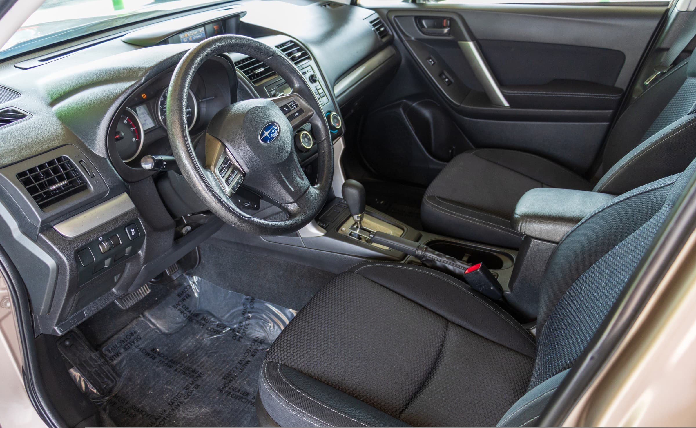Driver's cockpit of the Forester: black dashboard, leather-wrapped steering wheel and black cloth seats.