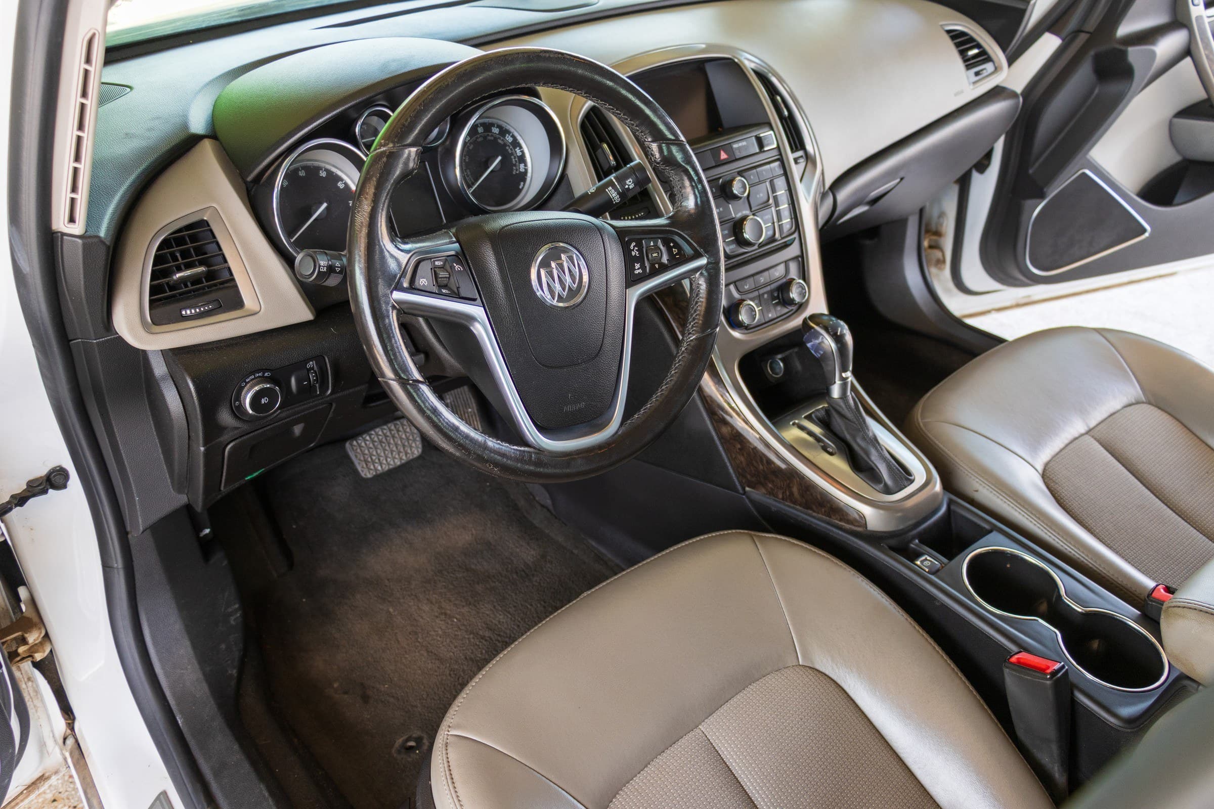 Driver's cockpit of the Verano: light grey leather seats, wood-grain console trim and a leather-wrapped steering wheel.