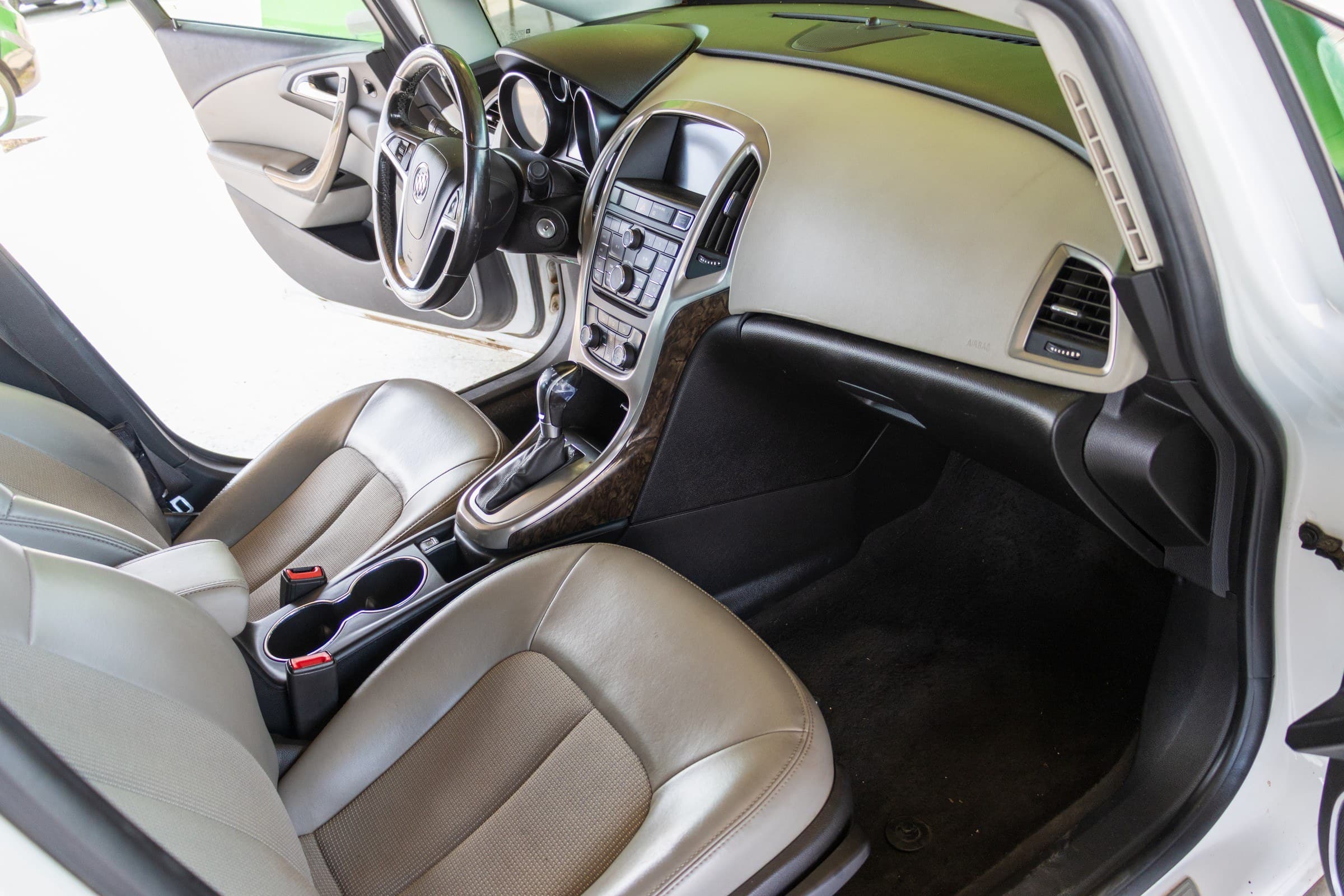 Verano interior seen through the open passenger door, showing the two-tone dashboard, centre stack and light grey seats.